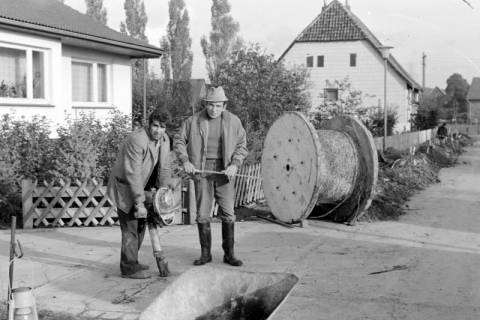 ARH Slg. Weber 02-128/0022, Zwei Männer bei der Vorbereitung eines Lochs für die Verlegung von Kabeln in einem Wohngebiet, zwischen 1980/1990