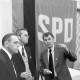 Archiv der Region Hannover, ARH NL Mellin 01-149/0019, Drei Männer in einem Gespräch vor einer Art Wandteppich mit dem Aufdruck "SPD"