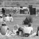 ARH NL Mellin 01-172/0017, Menschen auf einer Wiese vor einer Bühne sitzend