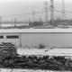 Archiv der Region Hannover, ARH NL Mellin 02-154/0016, Blick über eine eingezäunte Schafherde auf eine Halle und das dahinterliegende Elektrizitätswerk(?)