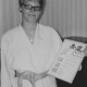 Stadtarchiv Neustadt a. Rbge., ARH Slg. Bartling 2073, Einzelporträt einer jungen Frau (S. Wiskemann) als Karateka im Karate-Gi mit hellem Gürtel, Brille tragend, eine Urkunde mit der Linken zeigend, in häuslicher Umgebung