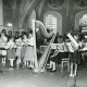 Stadtarchiv Neustadt a. Rbge., ARH Slg. Bartling 2160, Dora Kolesch (l.) beim Dirigat eines Jugendorchesters u. a. mit Blockflöten und Harfe im Altarraum der Kirche, Blick in die Apsis, Basse