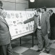 Stadtarchiv Neustadt a. Rbge., ARH Slg. Bartling 2252, Mehrere Männer beim Betrachten einer aufgestellten Tafel in einer Briefmarken-Ausstellung im FZZ, Neustadt a. Rbge.
