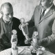 ARH Slg. Bartling 2292, Der 1. Vorsitzende der Sportschützen Fritz Jonat (r.) und N. N. begutachten fünf Pokale auf einem runden Tisch mit Häkeldecke, Neustadt a. Rbge.