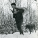 Stadtarchiv Neustadt a. Rbge., ARH Slg. Bartling 2483, Jagdpächter Dr. med. dent. Henning Gode mit Flinte, Fernglas, Rucksack und Hund im winterlichen Wald durch hohen Schnee zur Wildfütterung stapfend