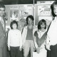 Stadtarchiv Neustadt a. Rbge., ARH Slg. Bartling 2829, N. N. von der Volksbank Neustadt gratuliert vier Schüler*innen, die vor einer Stellwand mit Kinderbildern stehen, Neustadt a. Rbge.
