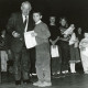 Stadtarchiv Neustadt a. Rbge., ARH Slg. Bartling 2891, Zahlreiche Grundschulkinder auf einer Bühne stehend mit einer Urkunde in der Hand, vorne Bürgermeister Henry Hahn mit einem Kind in die Kamera schauend, Neustadt a. Rbge.