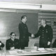 Stadtarchiv Neustadt a. Rbge., ARH Slg. Bartling 3322, Fritz Steege gratuliert dem Heinrich Schaper per Handschlag, beide stehend, im Lehrsaal; daneben sitzend: Grosse und Georg Meyer (l.) und Kreisbrandmeister Horst Dempewolf (r.), Wunstorf