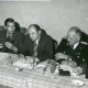 Stadtarchiv Neustadt a. Rbge., ARH Slg. Bartling 3329, Kreisdirektor Wolfgang Kunze (v. l.), Amtsrat Heinz Busse (Ordnungsamt) sowie uniformierte Feuerwehrleute N. N. und Henry Hahn am Vorstandstisch sitzend, Neustadt a. Rbge.