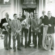 Stadtarchiv Neustadt a. Rbge., ARH Slg. Bartling 3559, Gruppenbild einer mit einem Blumenstrauß geehrten Blaskapelle von sieben Männern mitsamt Pastor N. N. im Talar vor dem Kanzelaltar der Evangelisch-lutherischen Kirche, Helstorf