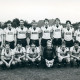 Stadtarchiv Neustadt a. Rbge., ARH Slg. Bartling 3763, Gruppenportrrät einer Herren Fußballmannschaft des TSV Poggenhagen im Trikot mit der Aufschrift "Colonia Peschel" nebeneinander auf einem Fußballplatz stehend, Poggenhagen