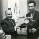 Stadtarchiv Neustadt a. Rbge., ARH Slg. Bartling 3830, Überreichung eines Blumengebindes an den Bürgermeister und Lehrer Rudolf Löffler (SPD) (rechts) durch den Bürgermeister a. D. Christian von Winkler (CDU) in einem Klassenzimmer, Poggenhagen
