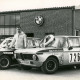 Stadtarchiv Neustadt a. Rbge., ARH Slg. Bartling 3871, Manfred Mineif, Rennfahrer aus Bordenau, vor einer Werkstatt mit BMW-Logo über der Eingangstür und zwischen zwei für den Motorsport getunten BMW 1800, auf der Motorhaube des ersten ein Siegerkranz, auf der des zweiten ein Pokal, Bordenau