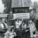 Stadtarchiv Neustadt a. Rbge., ARH Slg. Bartling 3987, "Dudensen. Ein Stück Natur." Ortseingangsschild, gestaltet im Rahmen des Wettbewerbs "Unser Dorf soll schöner werden". Eine Gruppe mit Familie posiert am Schild, Dudensen