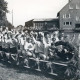 Stadtarchiv Neustadt a. Rbge., ARH Slg. Bartling 4069, Der größte Rodelschlitten der Welt, gebaut vom Ski-Club, besetzt mit zahlreichen Personen, versehen mit Rädern, auf einer grünen Weide, Eilvese