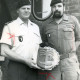 Stadtarchiv Neustadt a. Rbge., ARH Slg. Bartling 4342, Überreichung eines Kuchens in Form eines Wappens des PzBtl 33 an den Spieß der Kompanie, Stabsfeldwebel Adam Schmelzer (in sommerlicher Dienstuniform) durch Kompaniechef Hauptmann Busch (in Arbeitsuniform), Luttmersen
