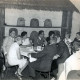 Stadtarchiv Neustadt a. Rbge., ARH Slg. Bartling 4376, Standortball im Soldatenheim Haus an der Jürse, Blick auf Tisch Nr. 5 mit zivilen und uniformierten Festteilnehmern vor einem Wandregal mit Bienenkörben, Luttmersen