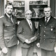 Stadtarchiv Neustadt a. Rbge., ARH Slg. Bartling 4431, Ehrung von drei Feuerwehrleuten, stehend vor einer mit Pokalen und Tellern gefüllten Vitrine, v. l. n. r.: Ortsbrandmeister Heinz Nebel, N.N., W. Oehlerking, Mandelsloh