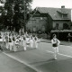 ARH Slg. Bartling 4479, Spielmannszug Mariensee beim Marsch durch den Ort, Blick über den Standartenträger, den Tambourmajor und den Zug auf die Bäckerei auf der anderen Straßenseite, Mariensee
