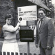 Stadtarchiv Neustadt a. Rbge., ARH Slg. Bartling 4529, Angestellte Helga Rübenhaus aus dem Büro und Christian Herr, damals 1. Vorsitzender des Verkehrsvereins, neben dem Firmenschild der Sprechstelle des Fremdenverkehrsbüro - Tourist-Information, Mardorf