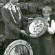 Stadtarchiv Neustadt a. Rbge., ARH Slg. Bartling 4648, Schützenkönig und Kinderschütze nebeneinander stehend und zwei Schützenscheiben präsentierend (links mit Wildschwein, rechts mit Eichelhäher) beim Schützenfest, Metel