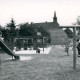 Stadtarchiv Neustadt a. Rbge., ARH Slg. Bartling 4743, Blick über die Spielgeräte (Rutsche und Klettergerüst) des Kinderspielplatzes auf die benachbarte alte Schule mit Dachreiter (2. Ex.), Nöpke