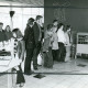 Stadtarchiv Neustadt a. Rbge., ARH Slg. Bartling 5034, Kinder mit Uniformierten des DRK aufgereiht stehend und auf einen Regalwagen schauend im Vorraum der Schulbücherei, Poggenhagen